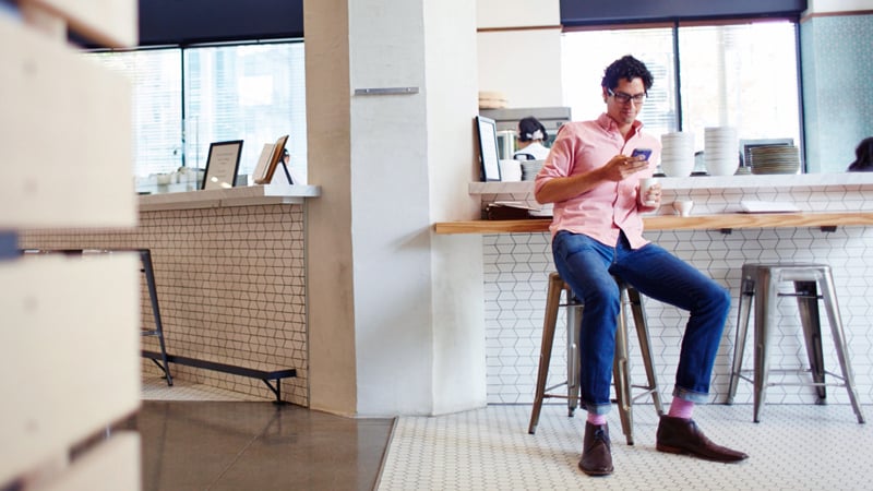 Man seated at café counter checking his phone.